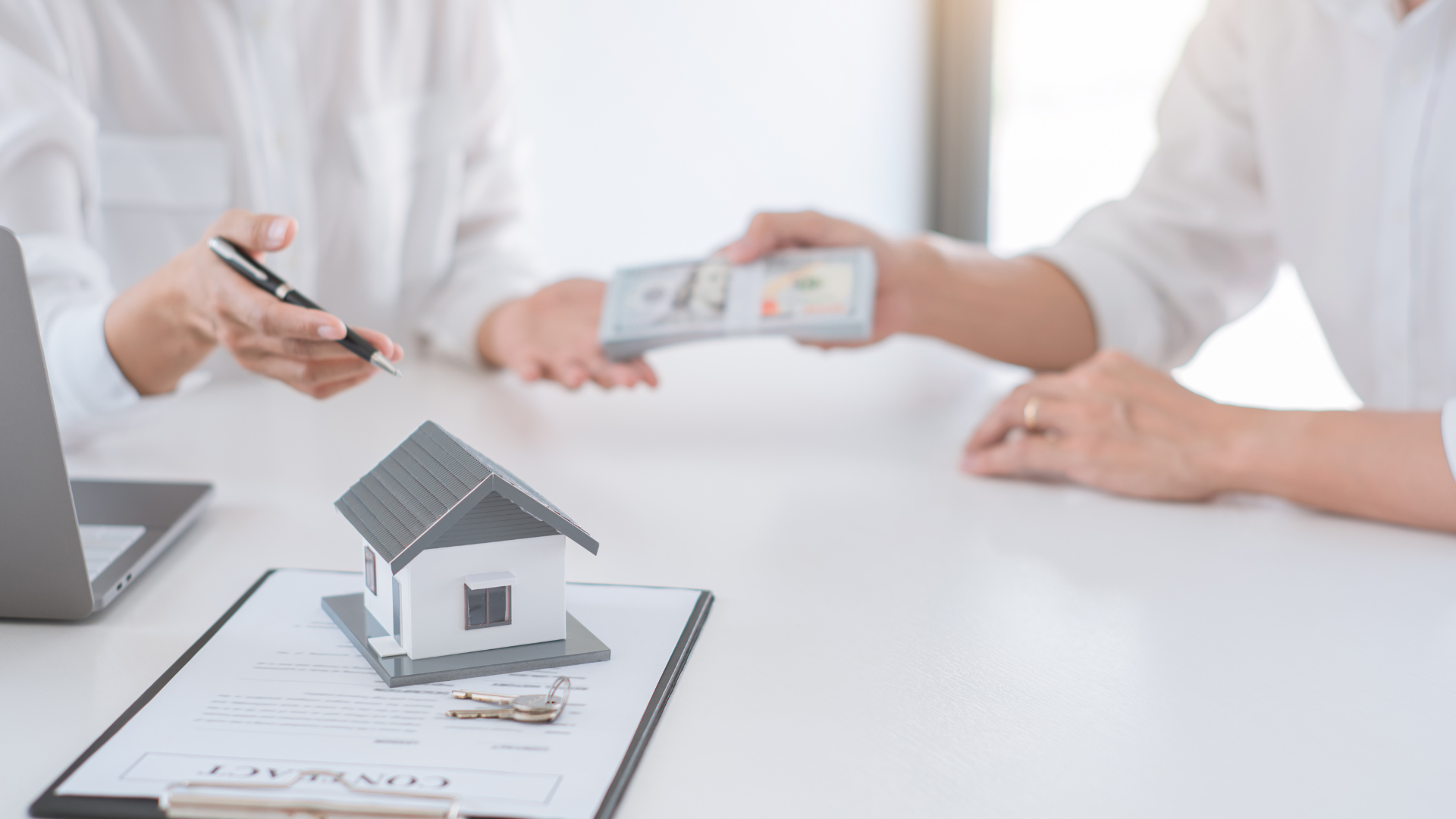 two people exchanging money across a desk with a small model of a house on it